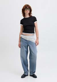 Black short-sleeve t-shirt with white trim, light blue loose-fitting jeans, white netted wrap around the waist, and black shoes. Green-tinted glasses.