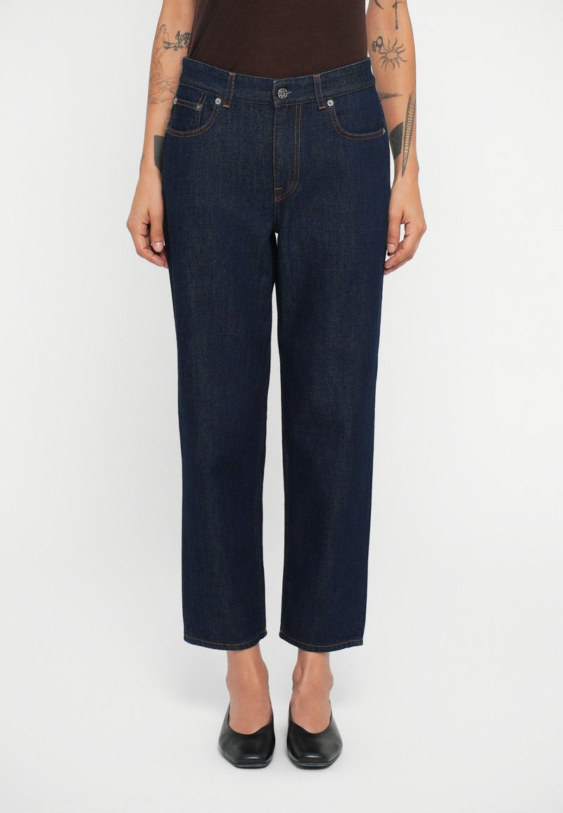 Jeans de mezclilla azul oscuro con corte recto, cinco bolsillos y cierre de botón. Presentan costuras naranjas y una cinturilla estándar.