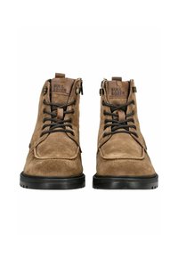 Hnědé semišové kotníkové boty s černými gumovými podrážkami, zdobené hnědými koženými detaily, předním šněrováním a bočními zipy pro snadné obouvání.