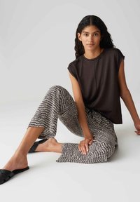 Haut marron foncé à manches courtes associé à un pantalon large noir et blanc à motifs. Le mannequin porte des sandales à semelles plates noires.