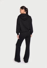 Set din hanorac cu glugă negru și pantaloni evazați, realizat dintr-un material moale. Prezintă o croială lejeră și manșete ribbate, evidențiind un design fără cusături.