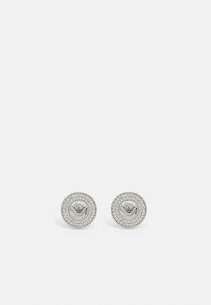Pendientes de plata con un diseño circular, que cuentan con un logotipo en el centro y un borde de cristales transparentes como acento.