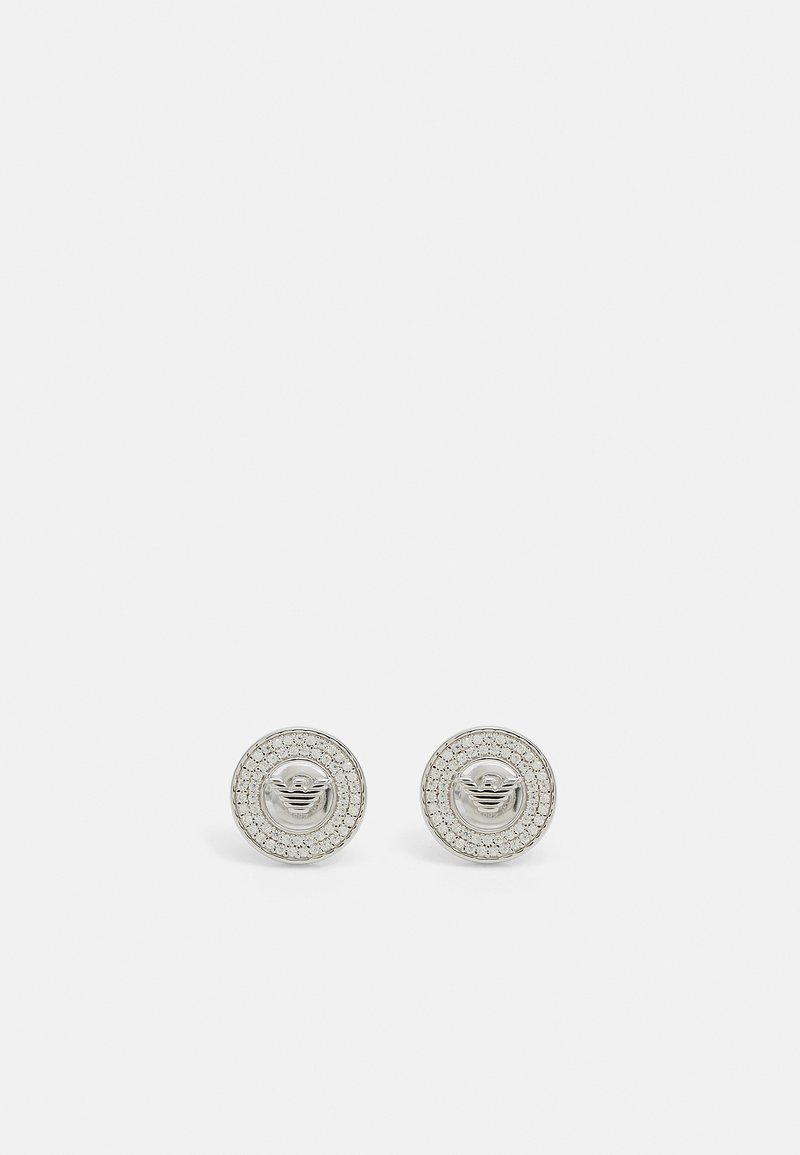 Pendientes de plata con un diseño circular, que cuentan con un logotipo en el centro y un borde de cristales transparentes como acento.