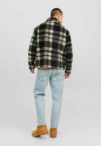 Giacca di pile a quadri nera e beige con colletto, abbinata a jeans azzurri e scarponi marroni, vista da dietro.