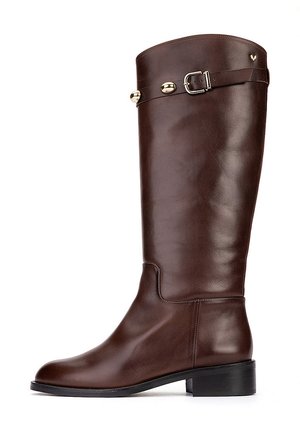 Bota marrón de cuero hasta la rodilla con tacón bajo, correa lateral con hebilla y tachuelas decorativas doradas sobre fondo blanco liso.