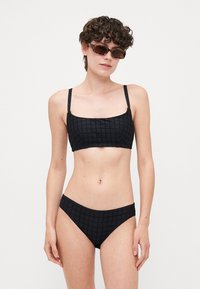 Svart bikini-set med en texturerad, rutad design. Topp med tunna justerbara band; botten har en klassisk skärning. Slät tyg.