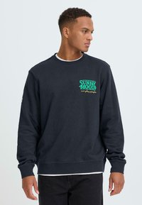Marineblauwe katoenen sweatshirt met een bedrukt "SUNNY MOOD" logo in groen en geel op de borst. Lange mouwen met geribbelde boorden.