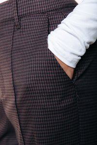Nohavice s károvaným vzorom v maroon a čiernej farbe so bočnou kapsou, skombinované s bielou košou s dlhým rukávom, predvádzajúce textúru látky.