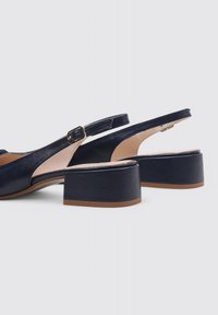 Chaussures à talon bas en cuir lisse de couleur bleu marine avec une bride arrière. Lanière de cheville ajustable avec une boucle dorée et design à bout ouvert.