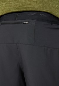 Șorturi atletice negre cu un buzunar cu fermoar, material texturat și logo-ul "NIKE RUNNING" pe talie.