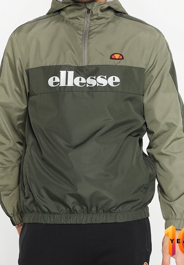 Olivově zelená větrovka s půl zipem, elastickými manžetami a lemem. Obsahuje bílé logo "ellesse" a nášivku loga na kapuci.
