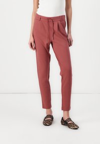 Dusty rose tapered pants with drawstring waist, side pockets, and subtle pleats, paired with black and leopard print flats.