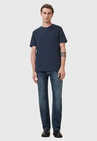 Camiseta de algodón azul marino de mangas cortas, combinada con jeans de corte recto, llevada con zapatos negros. Diseño sencillo sin patrones.