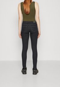 Jeans skinny de mezclilla negra con cintura media, que cuentan con bolsillos traseros y una textura suave. Combinados con una camiseta de tirantes verde con canalé.