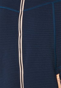 Mörkblå fleecejacka med texturerat tyg, kontrasterande dragkedja i ljusrosa och förstärkta sömmar med en modern passform.