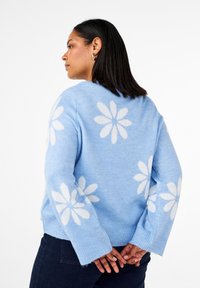 Hellblauer Pullover mit großen weißen Blumenmustern, gerippten Bündchen und lässiger Passform. Hergestellt aus weichem, strukturiertem Strickmaterial.