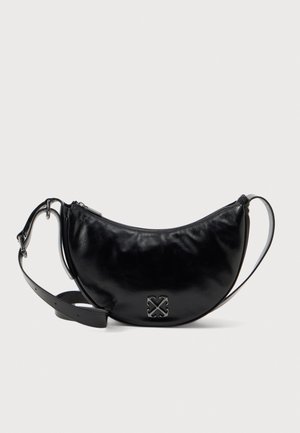Bolso bandolera de cuero negro con forma de media luna, correa larga ajustable, cierre de cremallera y emblema plateado de flechas cruzadas en la parte delantera.