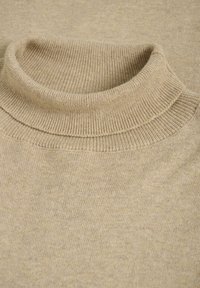 Pulover bej cu guler înalt, cu textură ribit, și tricot neted. Materialul pare moale și ușor. Design simplu, uniform.