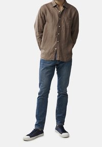 Hnědá lněná košile na knoflíky s kapsou, v kombinaci s modrými džíny a námořnickými teniskami s bílými podrážkami. Jednoduchý, přiléhavý design.
