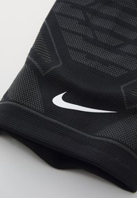 Svart Nike treningssleev med teksturerte diagonale mønstre. Har en fremtredende hvit swoosh-logo. Laget av et elastisk strikkemateriale.