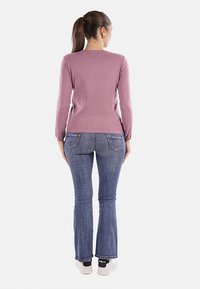 Maglietta rosa a maniche lunghe abbinata a jeans azzurri a zampa d'elefante e sneakers bianche. La maglietta ha un design aderente, mentre i jeans presentano tasche posteriori.