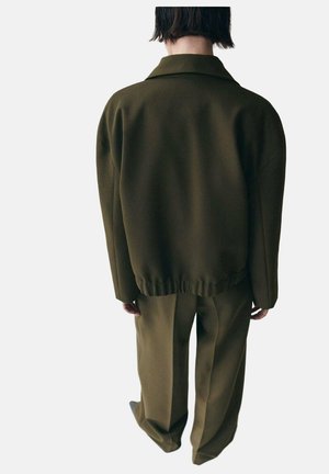 Giacca oversize verde oliva con colletto, tessuto testurizzato e vita elastica, abbinata a pantaloni a gamba larga coordinati.