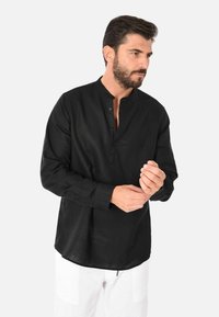 Camicia nera a maniche lunghe con colletto alla cinese, pattina con bottoni e vestibilità rilassata. Realizzata in tessuto leggero, presenta una superficie texture.