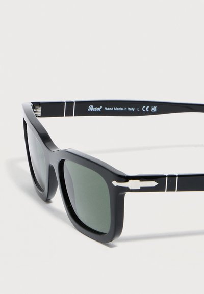 Μαύρα ορθογώνια γυαλιά ηλίου με σκουρόχρωμους φακούς, ασημένια λεπτομέρεια βέλους στα πλαϊνά, και κείμενο "Persol Χειροποίητο στην Ιταλία" στο μπράτσο.