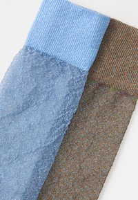 Due calzini strutturati: uno azzurro chiaro con un bordo a coste e un motivo glitterato, e uno marrone con una texture colorata e punteggiata.