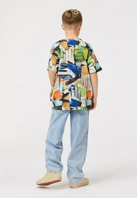 Värikäs graafinen T-paita, jossa on sekoitus abstrakteja muotoja sinisellä, vihreällä, oranssilla ja valkoisella; yhdistettynä vaaleansinisiin farkkuihin ja beigeihin kenkiin.