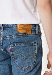 Jeans i denim med blåtvätt, med en läderlapp med varumärkets logotyp, gul sömnad och en liten röd logotagg på bakfickan.