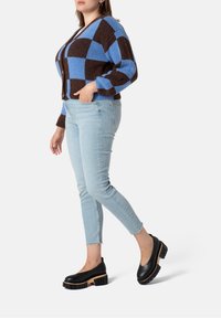 Blå och brun rutmönstrad kofta i kombination med ljusblå smala jeans och svarta plattformsskor med träsolar. Texturerat garnmönster synligt.