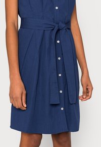 Navy-blaues Hemdkleid mit kurzen Ärmeln, einem taillierten Gürtel und einer glatten Textur. Verfügt über weiße Knöpfe und einen knielangen Saum.