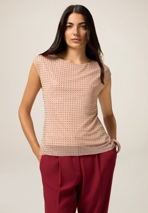 Top nudo con maniche corte, caratterizzato da un design testurizzato con borchie argentate. Il tessuto ha una superficie liscia e leggermente elasticizzata. Abbinato a pantaloni bordeaux.
