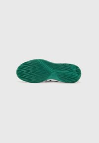 Schuhsohle mit grünem Gummiunterteil, das ein Zickzack-Profilmuster und glatte Abschnitte aufweist, übergehend zu einem weißen gepolsterten Oberteil.