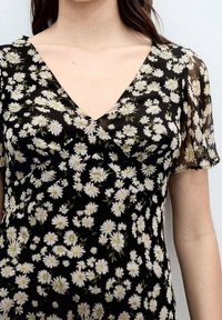 Vestido negro de flores con patrones de margaritas blancas, escote en forma de V y mangas flutter semitransparentes. Tejido ligero con una textura suave.