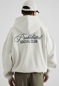 Felpa bianca con cappuccio ampio, caratterizzata da testo ricamato "Proibito" in corsivo e "SOCIAL CLUB" sottostante in lettere maiuscole. Vestibilità comoda.