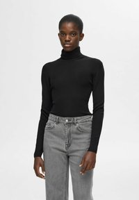 Zwarte ribbel turtleneck trui gecombineerd met lichtgrijze high-waisted jeans. De trui heeft lange mouwen en een aansluitend ontwerp.