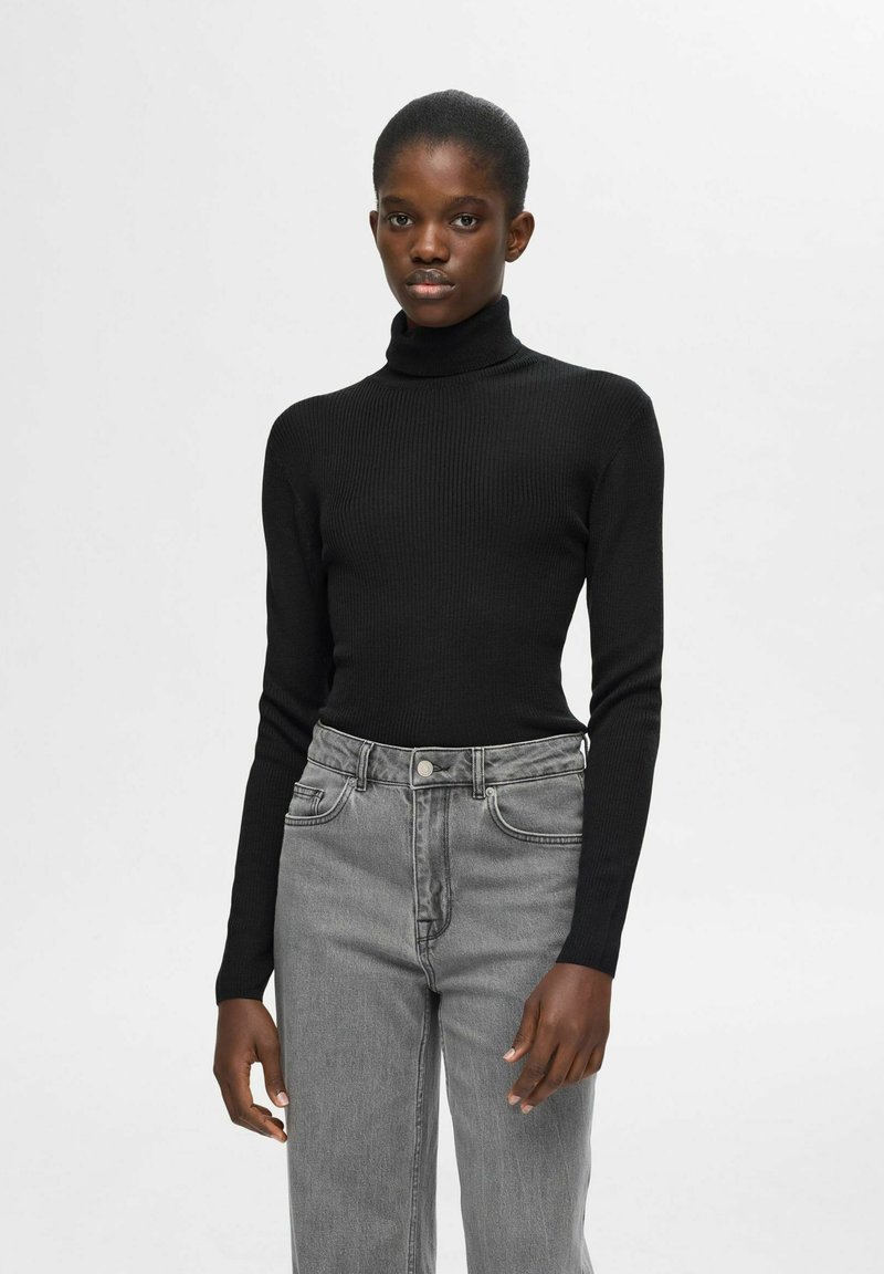 Zwarte ribbel turtleneck trui gecombineerd met lichtgrijze high-waisted jeans. De trui heeft lange mouwen en een aansluitend ontwerp.