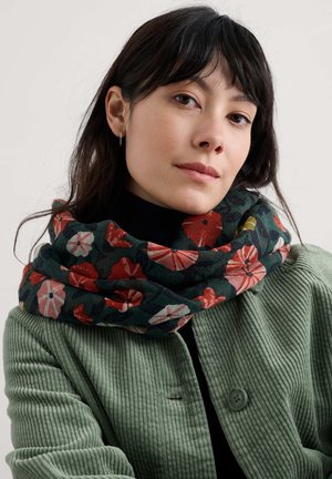 Sciarpa con motivo floreale in tonalità di verde, rosso e rosa, realizzata in tessuto morbido, avvolta in modo elegante attorno a un top nero, abbinata a un giacca in corda verde.