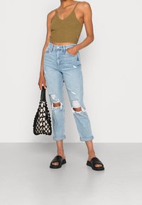 Cropped top a maglia verde oliva, jeans strappati a vita alta blu chiaro, sandali neri open-toe e una borsa a rete nera con fodera crema.