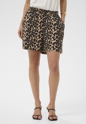 Kvinde iført leopardmønstrede shorts med elastik i taljen, hvid top, sorte sandaler med åben tå og guldarmbånd på højre håndled.