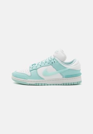 Lavtop sneaker i hvid og lys teal med Nike swoosh-logo, snørebånd, perforeret tå og gummisål, vist i sideprofil.