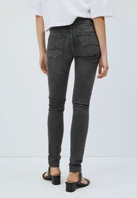 Svarta stretchiga jeans i skinny modell med bakfickor som har böjd sömnad, tillsammans med svarta klacksandaler med nitar.