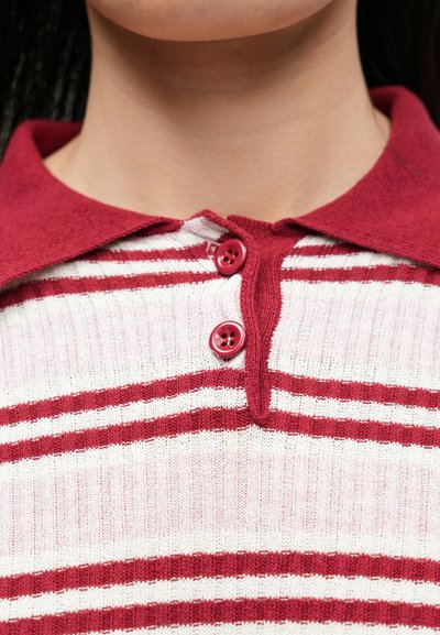 Pull rayé rouge et blanc à texture douce, avec un col à revers et deux boutons rouges, présentant un design décontracté.
