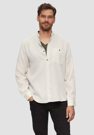 Lichtgekleurde, langmouwige blouse met een knoopsluiting, borstzak en zwarte knopen. Gedragen over een donkergroene V-hals shirt.