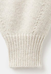 Detail bílé pletené svetr s žebrovaným manžetem a jemnou texturou. Příze má slabý lesk, což podtrhuje její jemný vzhled.