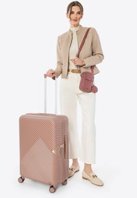 Roze harde koffer met diagonale ribbelstructuur, uitklapbare handgreep en vier wielen. Samen met een kleine schoudertas in een bijpassende tint.