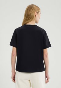 Czarna bawełniana koszulka z krótkimi rękawami, okrągłym dekoltem i luźnym krojem. Jednolity kolor, gładka tekstura i minimalistyczny design bez widocznych logo.