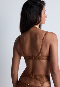 Soutien-gorge en dentelle marron avec motif géométrique, bretelles réglables et accents en métal doré, offrant une texture douce et un design raffiné.